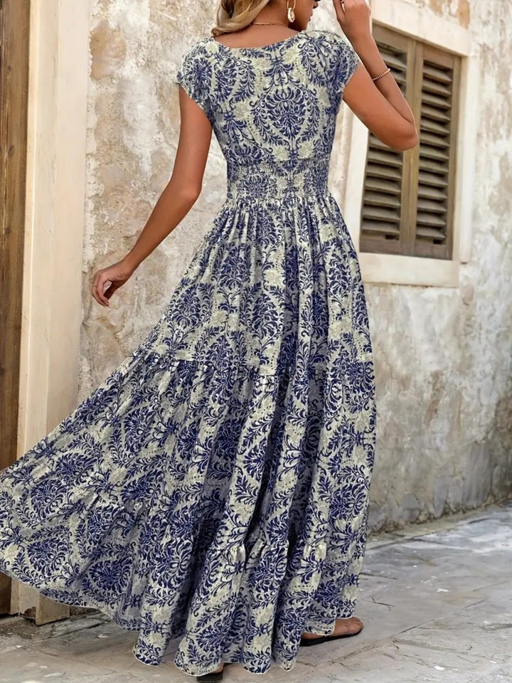 Woman wearing a blue floral dress standing against a stone wall.