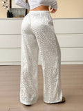 Person wearing white leopard print pants in a room with a wooden floor and light-colored walls.