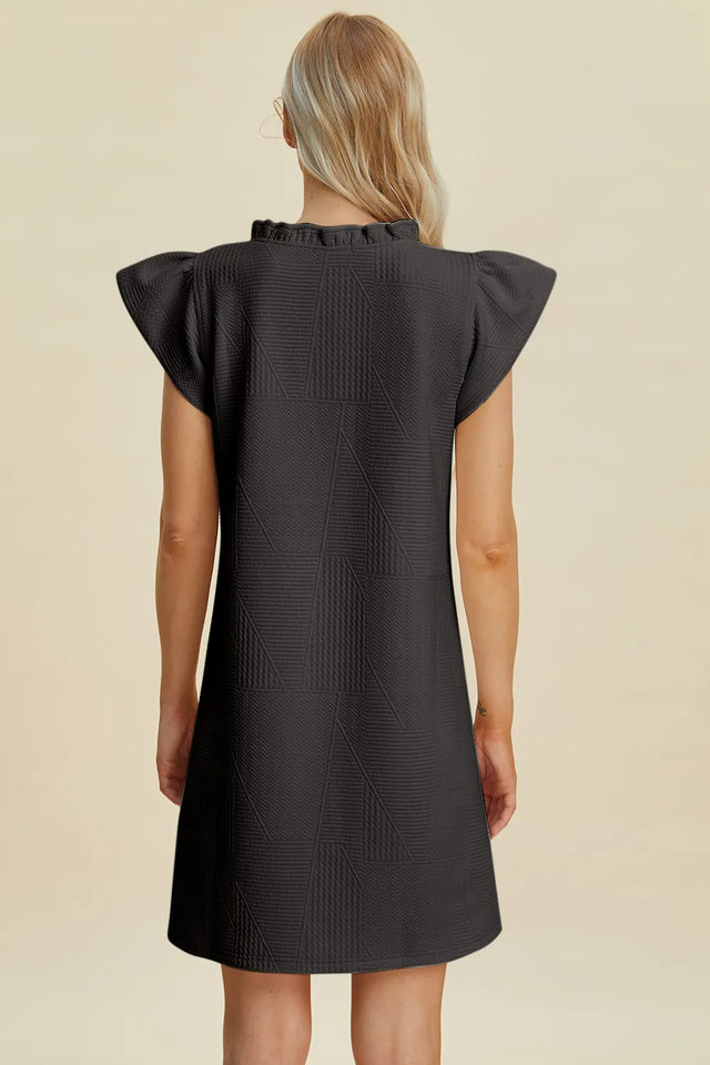 Black dress with ruffled sleeves worn by a person on a beige background