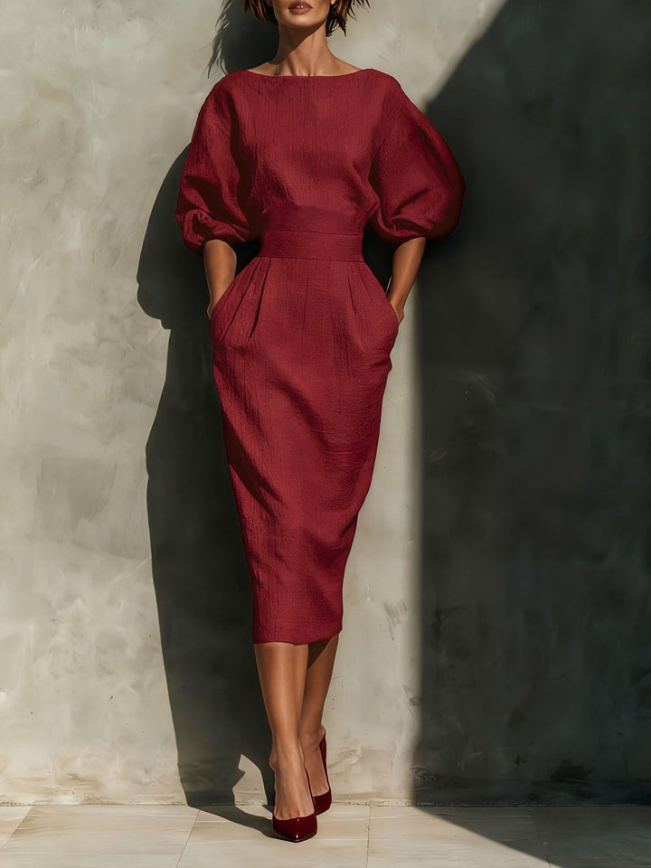 Woman wearing a red dress with puffed sleeves against a textured wall.