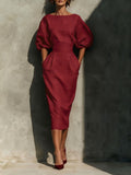 Woman wearing a red dress with puffed sleeves against a textured wall.