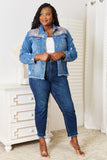 Woman wearing a blue denim jacket with floral embroidery and jeans in a room.