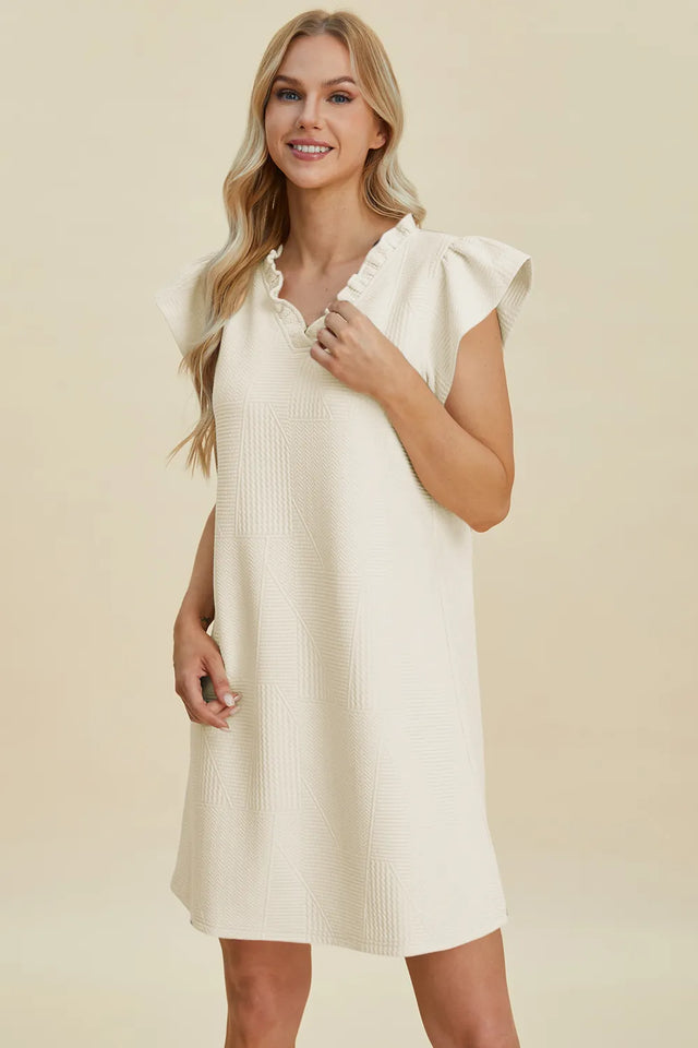 Woman wearing a white dress with ruffled sleeves against a beige background