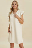Woman wearing a white dress with ruffled sleeves against a beige background