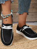 Black and white sneakers worn with denim jeans on a wooden floor.