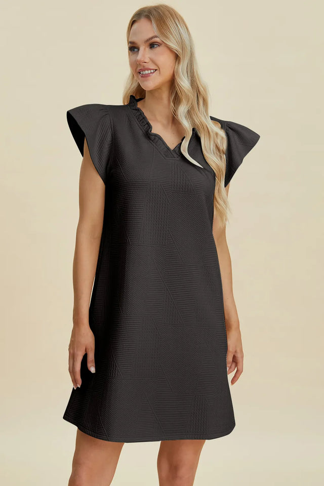 Woman wearing a black dress with ruffled shoulders on a beige background