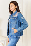 Woman wearing a blue denim jacket with floral embroidery on a white background