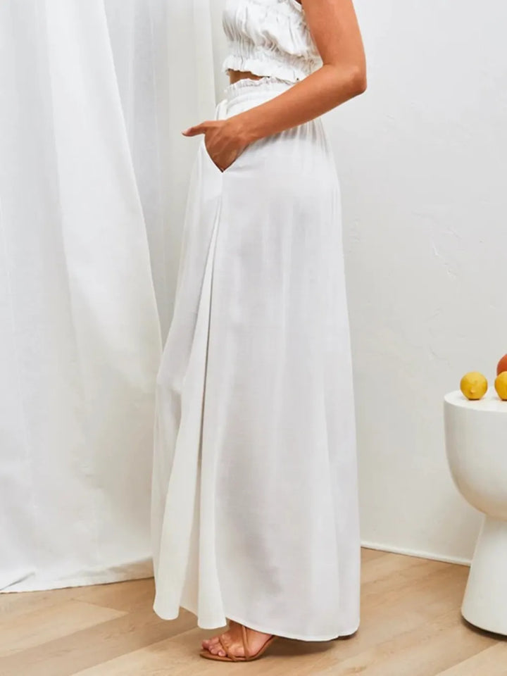 Person wearing a white dress standing in a minimalistic room with a white curtain and a small table with fruits.