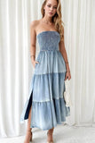 Woman wearing a strapless, tiered denim dress against a white curtain background