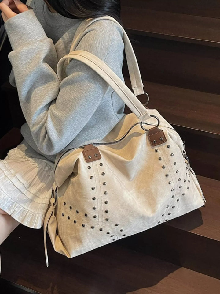 Beige handbag with brown accents held by a person sitting on steps.