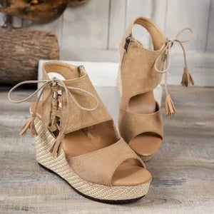 Black wedge sandals with tassels worn by a person, with a blurred background.