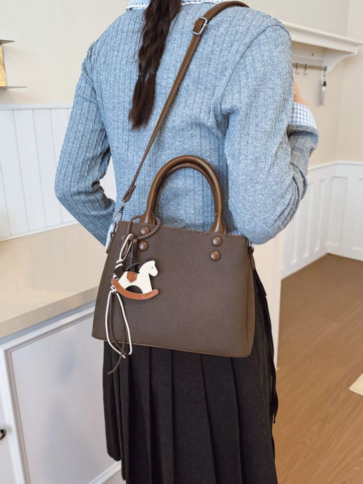 Person wearing a blue sweater and dark skirt with a brown handbag featuring a horse emblem.