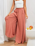 Person wearing pink wide-leg pants and a white top, standing in a room with a white curtain and fruit on a table.