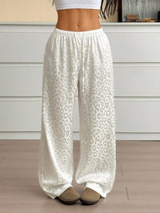 White satin pants with leopard print pattern worn by a person indoors.
