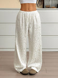 White satin pants with leopard print pattern worn by a person indoors.