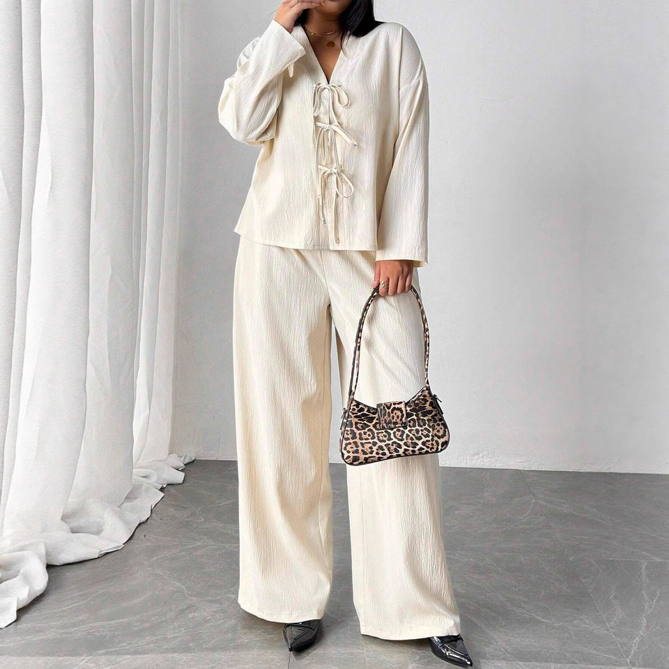 Person wearing a cream-colored outfit with a leopard print handbag against a white curtain background