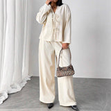 Person wearing a cream-colored outfit with a leopard print handbag against a white curtain background